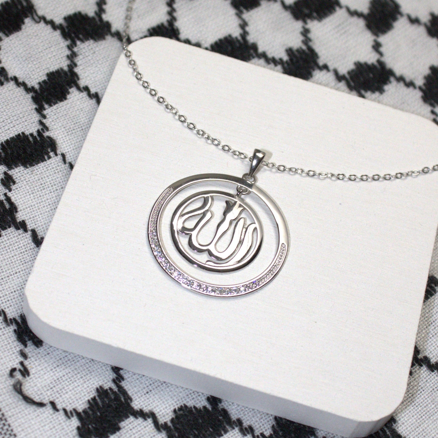 Silver necklace with a pendant on a white card against a black and white keffiyeh background