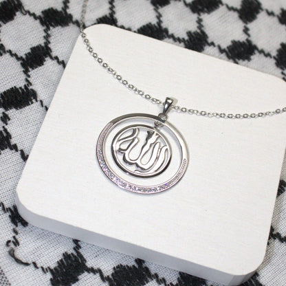 Silver necklace with a pendant on a white card against a black and white keffiyeh background

